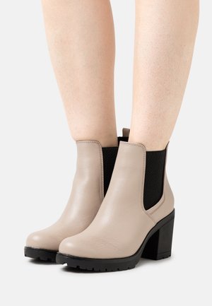 Beige læderankelstøvler med en kraftig sort hæl, elastiske sidelapper og en tekstureret sål for greb. Glat finish, rund tå.