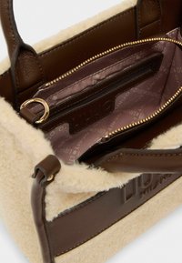 Sac à main en cuir marron avec des bordures en fausse fourrure crème et du matériel en ton or. L'intérieur comprend une poche zippée et un revêtement à motif de logo.