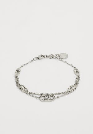 Pulsera de cadena de plata con tres cadenas interconectadas, que cuenta con acentos de logo y un cierre de broche. Incluye un pequeño colgante redondo.