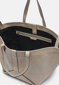 Beige Leder Einkaufstasche mit stabilen Griffen, einem schwarzen Innenraum und einer Reißverschlusstasche im Inneren. Mit geprägtem Logo auf der Außenseite.