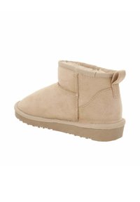 Una bota de tobillo de ante color arena con punta redondeada, tacón bajo y con detalles cosidos, forrada de suave material y con una lengüeta en la parte posterior.