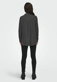 Langärmliges, dunkelgraues Hemd mit Knopfleiste und gefaltetem Rücken, kombiniert mit schwarzen Leggings und Stiefeln mit Knöchelschnitt. Glatte Textur, lockere Passform.