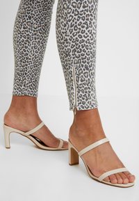Leggings de estampado de leopardo con detalle de cremallera en el tobillo, hechos de tejido elástico. Combinados con sandalias de tacón nude con dos tiras.