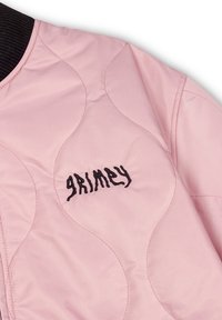 Roze gewatteerde jas met zwarte ribgebreide kraag; heeft de geborduurde tekst "grimy" in een gestileerd lettertype. Glad oppervlak en ronde naden.