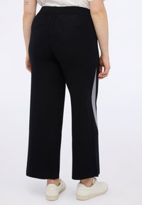 Zwarte wijde broek met een gladde textuur, voorzien van een grijze zijkant. De tailleband is elastisch en ze zijn gecombineerd met witte sneakers.