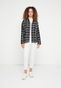 Koszula flanelowa w czarno-białą kratę, noszona na białej bluzce, w połączeniu z białymi zwężanymi spodniami i białymi trampkami. Prosty krój, luźne dopasowanie.