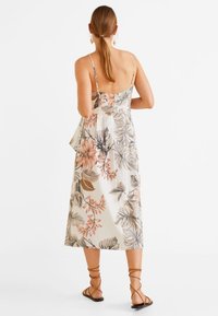 Kukallinen midi-mekko ohuilla olkaimilla, kerma värinen kangas, jossa on vaaleanpunaisia ja ruskeita lehvistökuvioita, sekä leveneviä detailleja takana. Ruskeat nauhaketjut.