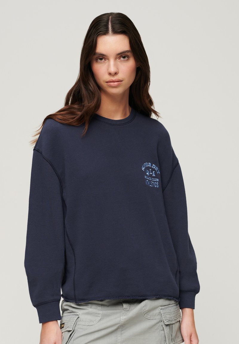 Felpa blu navy con scollo a girocollo, spalle scese e una piccola stampa grafica sul petto. Tessuto morbido con una vestibilità comoda.