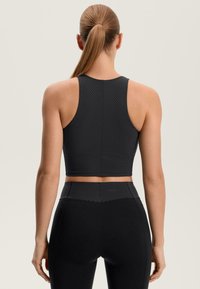 Čierny krátky športový top so štruktúrovaným vzorom rybej kosti, doplnený o čierne legíny s vysokým pásom a hladkým povrchom.