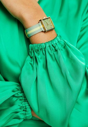 Quadratische Golduhr mit mintgrünem Ziffernblatt, Stoffarmband in Hellgrau mit gelben und blauen Streifen. Am Handgelenk mit gerafftem grünem Stoff getragen.