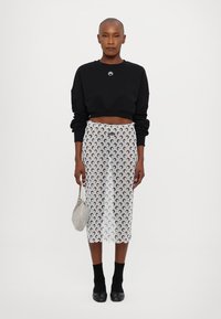 Black cropped sweatshirt, transparent skirt with crescent moon pattern, black socks, and heeled shoes. Gray handbag with textured surface.