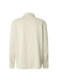 Chemise à manches longues avec col, de couleur beige clair, présentant une texture lisse, une coupe droite et des coutures discrètes sur le yoke arrière.