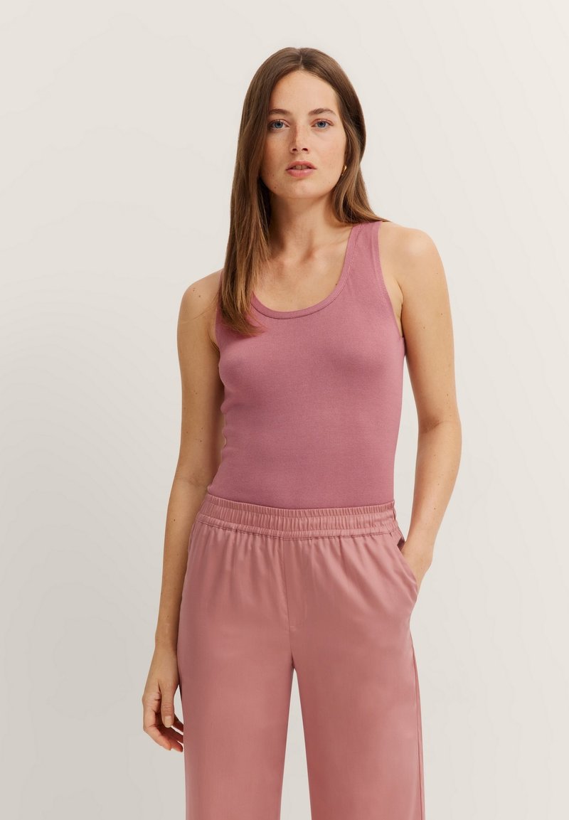 Light pink fitted tank top with a scoop neckline and soft texture, paired with loose pink trousers featuring an elastic waistband and side pockets.