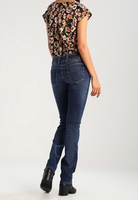 Niebieskie dżinsy o prostym kroju, z średnim stanem i tylnymi kieszeniami. Noszone z kwiecistą bluzką z krótkim rękawem i czarnymi botkami.