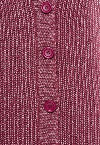 Stickad kavaj i djup burgundy med glänsande silvertrådar. Har fyra stora lila knappar framtill och en texturerad vävdesign.