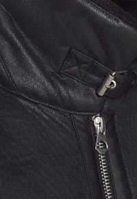 Svart skinnjacka med texturerad yta, dragkedjestängning och quiltad detalj vid kragen för extra stil.