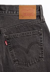 Jeans de mezclilla gris oscuro con una etiqueta de cuero que dice "Levi Strauss & Co." Cuentan con un bolsillo trasero con costura curva y una etiqueta roja.