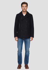 Caban en laine bleu marine foncé avec boutons croisés, deux poches latérales et col à revers, associé à un jean bleu clair et des chaussures en cuir marron.