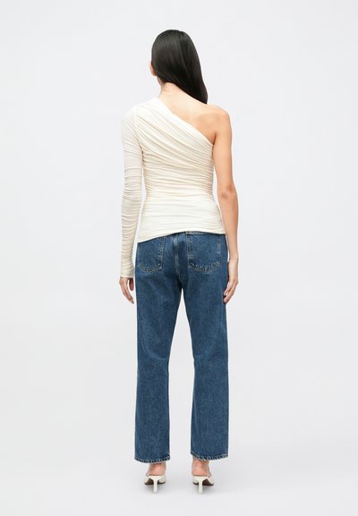 Top creme assimétrico com textura franzida num dos lados, combinado com jeans de perna reta azuis e saltos claros.