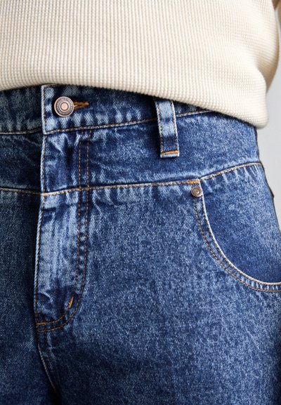 Denim jeans with a mid-rise waist, blue color, contrasting orange stitching, and a copper button detail at the waistband.