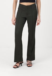 Dark green ribbed flared pants with a mid-rise waistband, featuring vertical seams and a smooth texture, paired with black strappy heels.