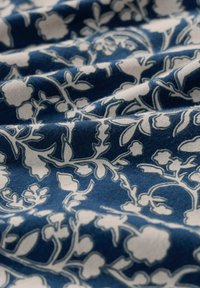 Marineblauem Stoff mit einem zarten weißen Blumendesign, das verwobene Äste und kleine Blüten zeigt. Weiche Textur mit einem subtilen Glanz.