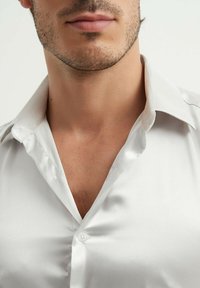 Chemise blanche en satin avec un col pointu, présentant un devant à boutons et une texture lisse, vue en gros plan montrant les détails du col et du cou.