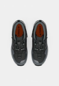 Must musta ja hallid Adidas Terrex matkajalatsid punaste sisesoolte ja kiire pingutussüsteemiga, vaadatuna ülevalt valgel taustal.