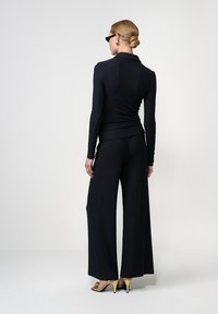 Čierny rebrovaný pletený top s vysokým golierom, doplnený zodpovedajúcimi širokými nohavicami. Detailne doplnený o elegantné, lesklé zlaté topánky na vysokých podpätkoch.