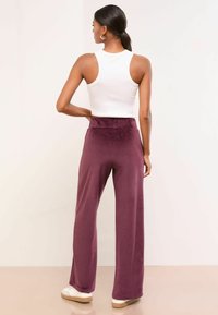 Weite Hosen aus tiefburgunderrotem Velvet, kombiniert mit einem taillierten weißen Tanktop. Glatte Textur mit hoher Taille und minimalen Akzentdetails.