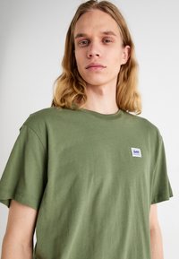 T-shirt in cotone verde oliva con maniche corte, caratterizzato da una piccola etichetta con il logo Lee sul lato sinistro. Design semplice con collo a giro e una texture morbida.