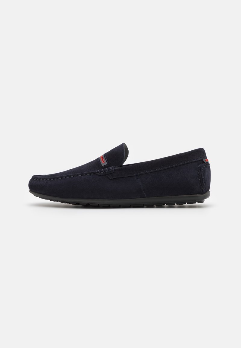 Mocassin homme en daim bleu marine avec semelle en caoutchouc noire et discrète étiquette logo rouge sur la tige et le talon.