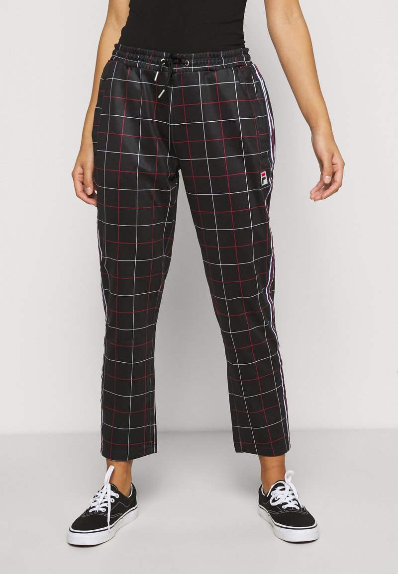 Personne portant un pantalon noir à motif quadrillé rouge et blanc avec des bandes latérales, assorti à des baskets noires et blanches à lacets.