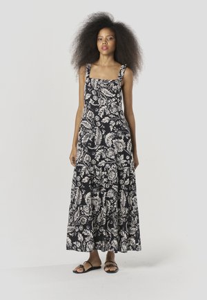 Zwart-witte bloemen maxi-jurk met vierkante halslijn, brede bandjes en gelaagde rok. Stof toont gedetailleerde patronen van bladeren en bloemen.