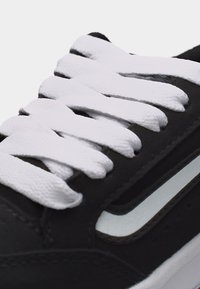 Κοντινό πλάνο μαύρου αθλητικού παπουτσιού που δείχνει λευκά υφασμάτινα κορδόνια δεμένα μέσα από τρύπες και μια λευκή καμπυλωτή ρίγα στη πλευρά.