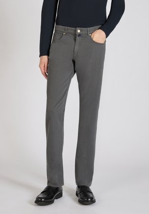 Grijze herenbroek met een slim fit, voorzien van een knoopsluiting, zijzakken en een gladde textuur. Gecombineerd met zwarte instappers.