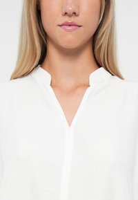 Witte blouse met een V-hals en ronde kraag. Heeft een soepele textuur en nette stiksels, ontworpen voor een casual pasvorm.