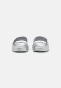 Sandali scivolati argentati con punta aperta, parte superiore curva e strutturata, suola piatta e finitura distintiva e liscia. Design leggero, adatto per un abbigliamento informale.