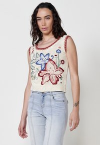 Top de punto sin mangas en crema con bordado floral en azul, rojo y verde. Presenta un escote redondo y bordes texturizados.