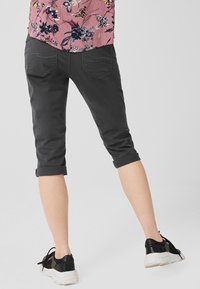 Pantalons gris foncé coupés avec des ourlets retroussés, dotés de poches latérales et d'une texture lisse, associés à des baskets noires. Chemise à motifs floraux partiellement visible.