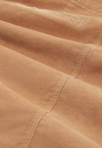 Tissu texturé beige avec de fines rainures, présentant des coutures brodées pour la structure. La surface semble lisse avec un léger éclat.