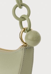 Bolsa de mão de couro verde com um acabamento texturizado, ferragens douradas e uma alça de corrente grossa com um charme circular. Fecho de zíper na parte superior.
