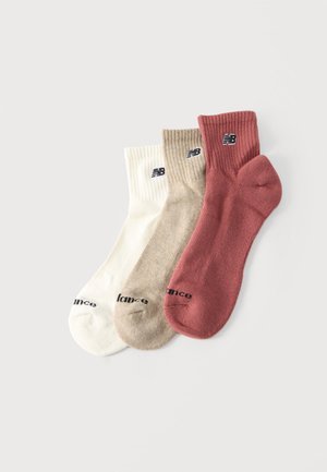 Trois paires de chaussettes New Balance à tige courte en blanc, beige et rose poussiéreux, posées à plat et légèrement superposées sur un fond blanc.