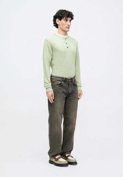 Light green long-sleeve henley shirt with three buttons, paired with dark grey jeans. Shoes are two-tone with a brown accent.