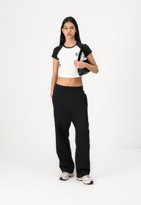 Svart og hvit cropped t-skjorte med korte ermer og grafikk, paret med løse svarte bukser. Modellen holder en liten svart veske.