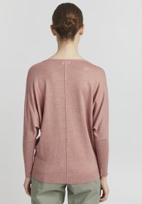 Maglione rosa svasato con scollo rotondo, spalle cadenti e dettaglio della cucitura centrale sul retro. Tessuto lavorato a maglia, texture morbida.