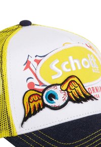 Casquette de baseball blanche et jaune avec des côtés en mesh. Présente un design brodé d'un œil avec des ailes et le logo "Schott" en jaune. Visière en denim bleu.