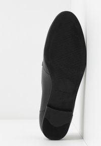 Semelle de chaussure habillée en cuir noir avec une adhérence texturée, nom de la marque « Vagabond » et taille 37 embossés sur la zone du talon.