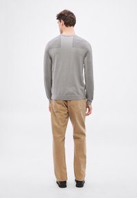 Pulover gri cu mâneci lungi, cu textură tip tiparete, decolteu rotund și panouri distincte pe umeri, combinat cu pantaloni bej cu croială dreaptă și pantofi negri.