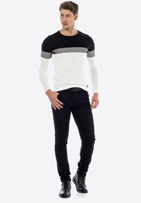 Gebreide trui met zwart-witte horizontale strepen, gestructureerde stof, ronde halslijn, gecombineerd met zwarte slim-fit broeken en zwarte laarzen.